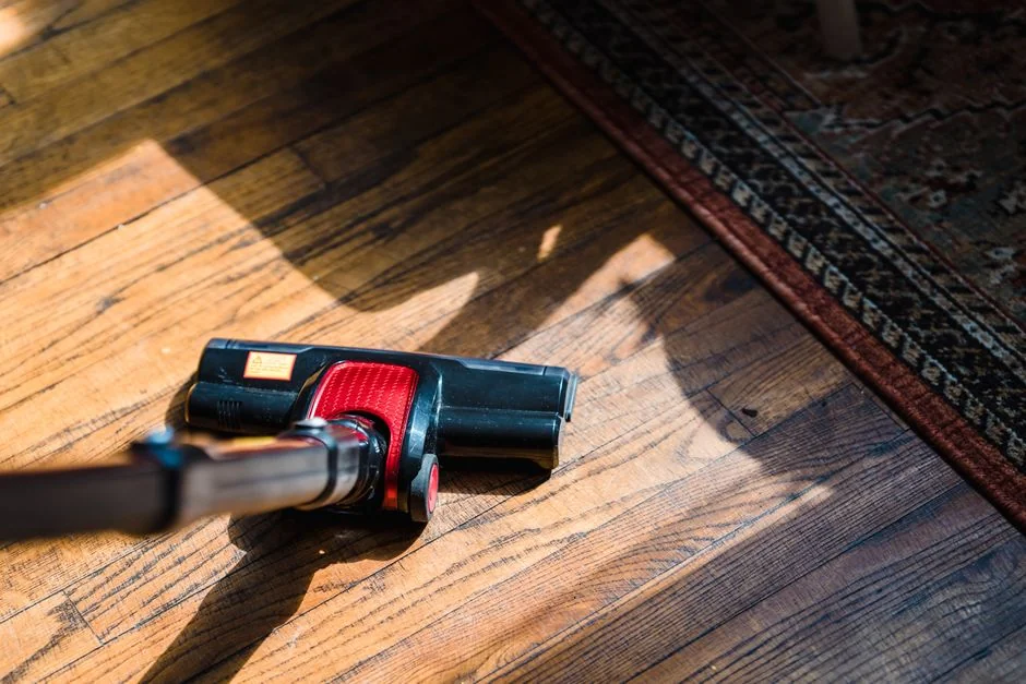 Two women in work clothes cleaning a modern living room using a vacuum and mop.